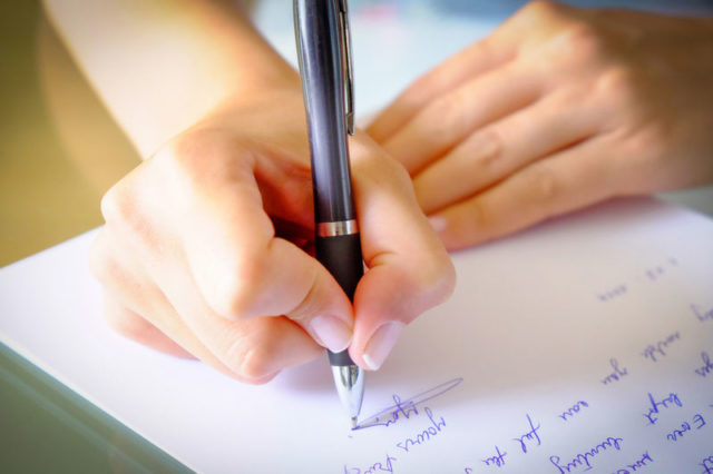 Female hand writing a hardship letter to her bank